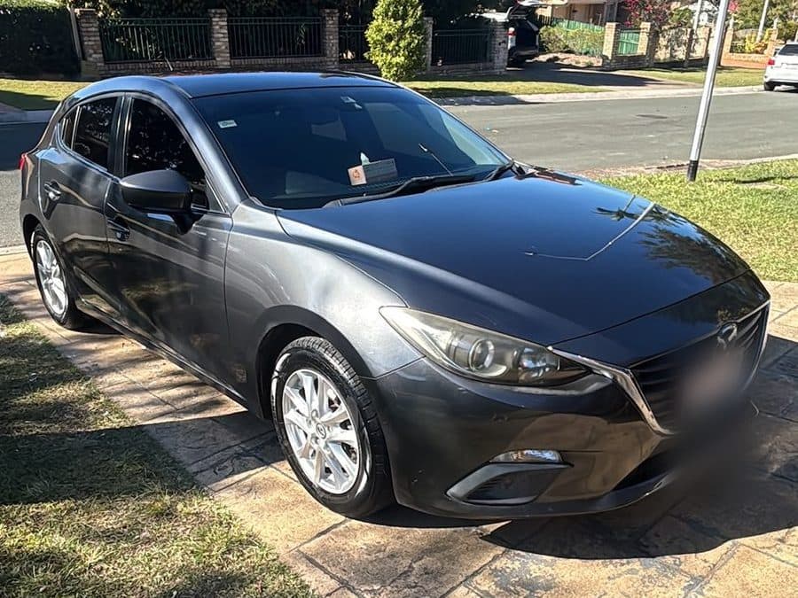 Dark grey 2013 Mazda 3 hatchback parked beside a lawn